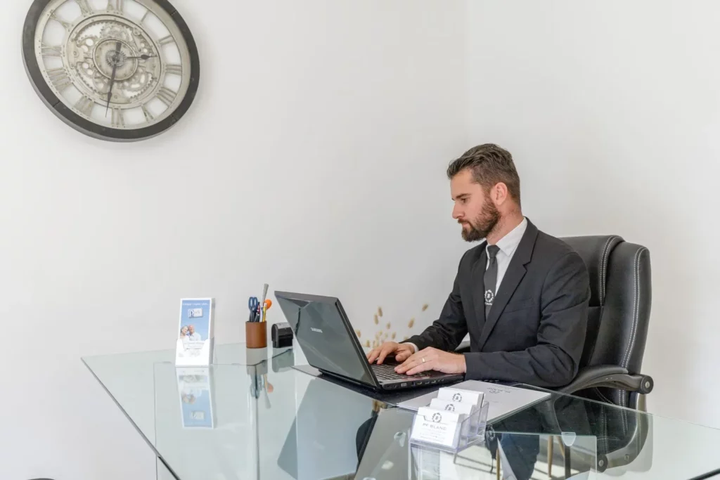 Conseiller funéraire PF Blanc assis à son bureau devant un ordinateur portable.